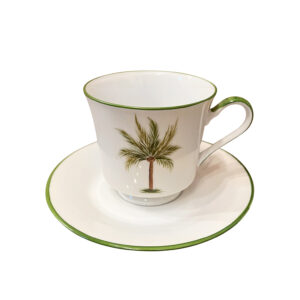 A white teacup with a palm tree design sits on a matching saucer.