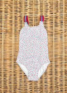 A floral-patterned one-piece swimsuit with pink straps on a woven surface.