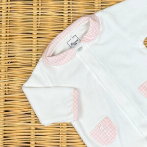 White baby onesie with pink gingham collar and pockets, placed on a woven surface.
