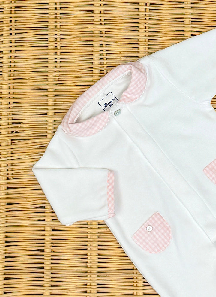 11471bianco_rosa_3_720x White baby onesie with pink gingham collar and pockets, placed on a woven surface.