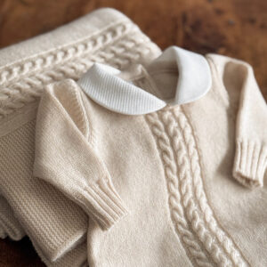 A cream-colored knitted sweater with a white collar, folded beside a matching blanket.