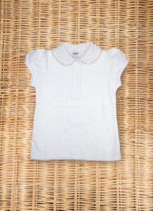 White short-sleeve polo shirt with a ruffled collar, laid flat on a woven surface.