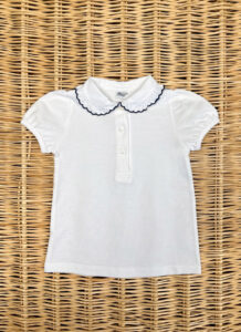 White short-sleeve polo shirt with a ruffled collar and three buttons, laid flat on a woven surface.