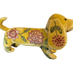 A yellow velvet dachshund with floral embroidery stands on a black background.