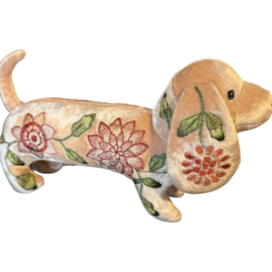 A plush dachshund with floral embroidery in pink and green, standing on a black background.