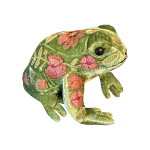 A green velvet frog with floral embroidery sits on a black background.