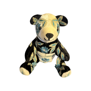 Small silk velvet bear with black and white fur, adorned with blue floral embroidery, sits upright.