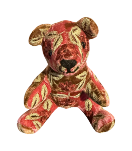 A plush bear with a red and gold floral velvet pattern, sitting upright with a friendly expression.