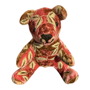 A plush bear with a red and gold floral velvet pattern, sitting upright with a friendly expression.