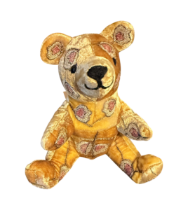 Small bear plush toy with golden velvet and floral patterns, sitting upright with a friendly expression.