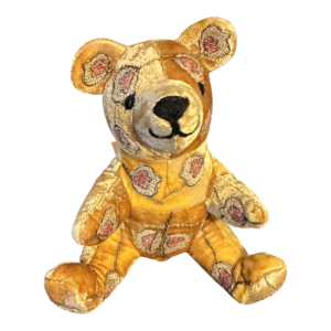 Small bear plush toy with golden velvet and floral patterns, sitting upright with a friendly expression.