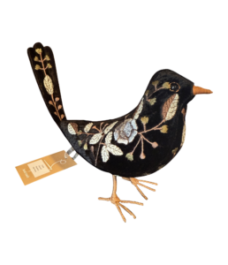 A black velvet bird with floral embroidery and a tag, standing on thin, woven legs.