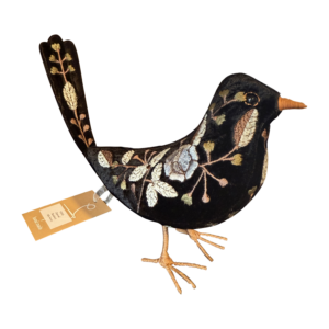 A black velvet bird with floral embroidery and a tag, standing on thin, woven legs.