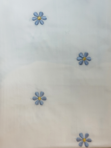 Light fabric with embroidered blue flowers and yellow centers scattered across the surface.
