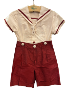 Sailor-style outfit featuring a white top with red trim and matching red shorts, displayed on a hanger.