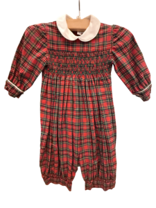 Red tartan long romper with a white collar and smocked bodice, hanging on a wooden hanger.