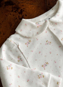 White fabric with small pink floral patterns and a rounded collar.