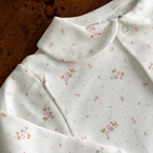 White fabric with small pink floral patterns and a rounded collar.