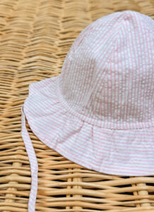 A pink and white striped sun hat rests on a woven surface.