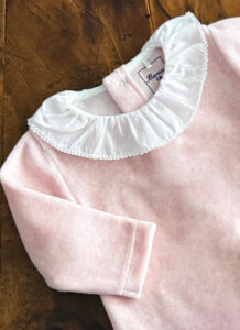 Light pink garment with a white ruffled collar, displayed on a wooden surface.