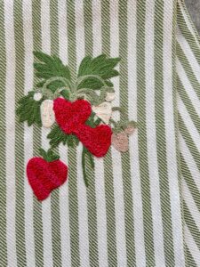 Embroidered strawberries and leaves on a striped fabric background.