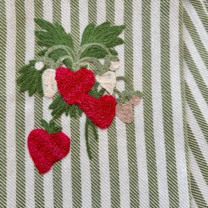 Embroidered strawberries and leaves on a striped fabric background.