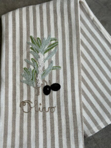 Embroidered olive branch and black olives on a striped fabric napkin. The word "Olive" is stitched below.