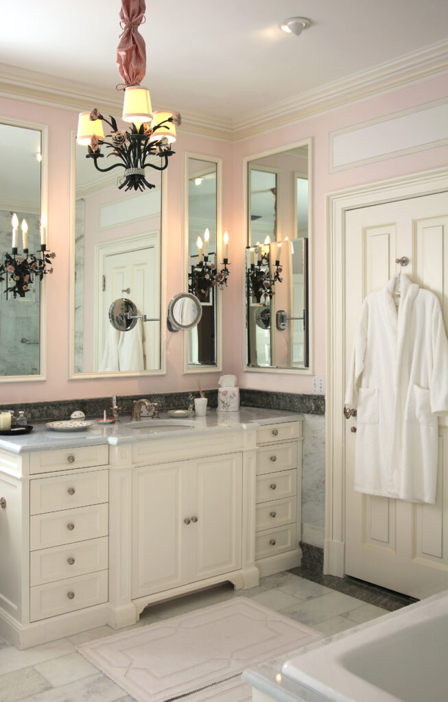 Elegant bathroom featuring a white vanity, marble countertops, mirrors, and a plush white robe hanging on the door.