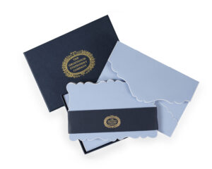 A navy box contains light blue stationery with decorative edges and a gold logo.