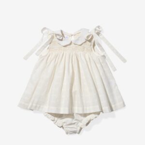 Cream-colored baby dress with a collar, smocked bodice, and ribbon ties, paired with matching bloomers.