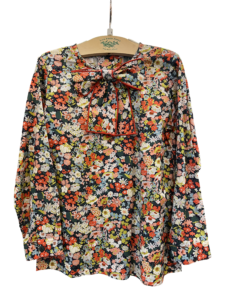 Floral blouse with long sleeves and a bow at the neckline, displayed on a hanger.