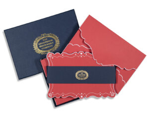 Navy box with gold logo contains red stationery with decorative edges and a navy band.
