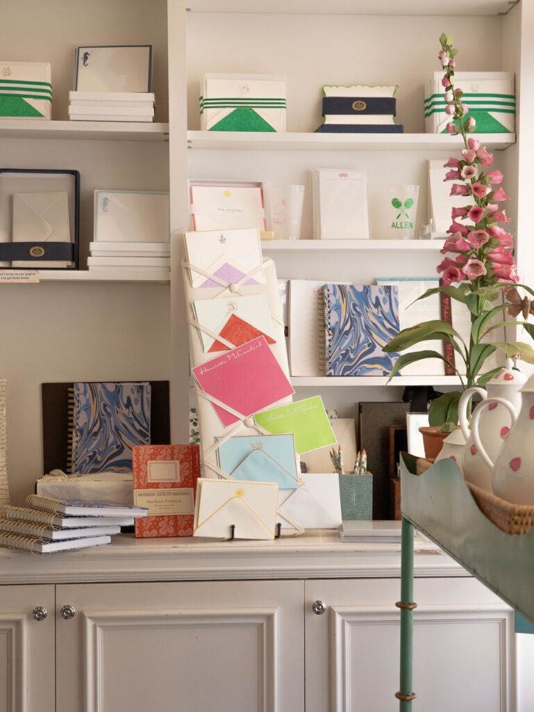 Colorful stationery and notebooks displayed on shelves, with a potted plant and teapot in the foreground.