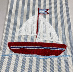 Red sailboat with white sails and a blue flag, embroidered on striped fabric.