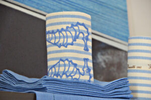Blue and white striped fabric rolls with embroidered seahorse designs, stacked with matching napkins.