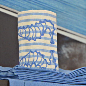 Blue and white striped fabric rolls with embroidered seahorse designs, stacked with matching napkins.