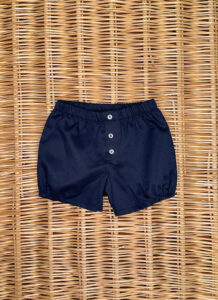 Navy blue shorts with an elastic waistband and three buttons, placed on a woven surface.