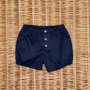 Navy blue shorts with an elastic waistband and three buttons, placed on a woven surface.