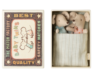 A matchbox contains two plush baby mice dressed in colorful outfits, nestled in a striped blanket.