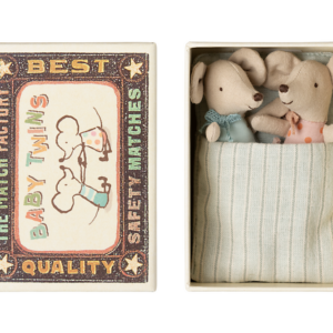 A matchbox contains two plush baby mice dressed in colorful outfits, nestled in a striped blanket.