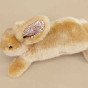 A plush rabbit with floral-patterned ears lies on a beige surface.