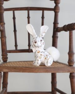 A decorative fabric bunny with a fluffy tail sits on a wooden chair.