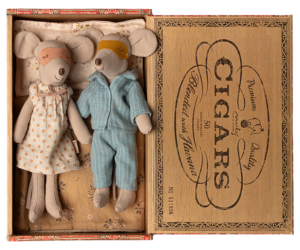 Two plush mice in pajamas and a nightgown rest in a vintage cigar box, surrounded by soft bedding.