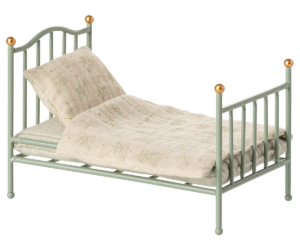 A small, green metal bed with a patterned blanket and two pillows.