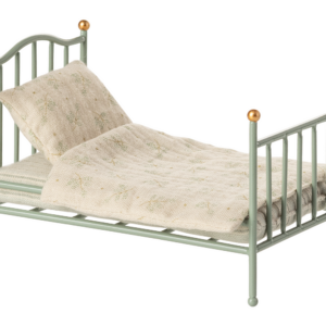 A small, green metal bed with a patterned blanket and two pillows.