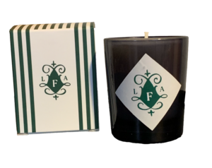 A dark candle with a decorative label, next to a striped box featuring the initials "LFA.