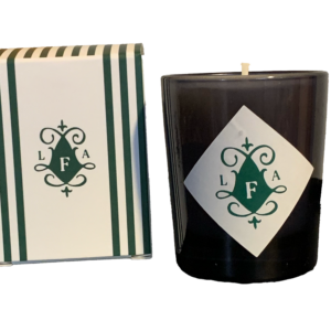 A dark candle with a decorative label, next to a striped box featuring the initials "LFA.