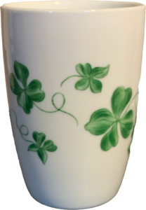 White cup decorated with green clover leaves and vines.