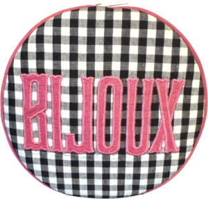 Round pouch with black and white checkered pattern and pink "BIJOUX" lettering.