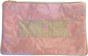 Pink cosmetic bag with "SKINCARE" embroidered in gray letters on a striped background.
